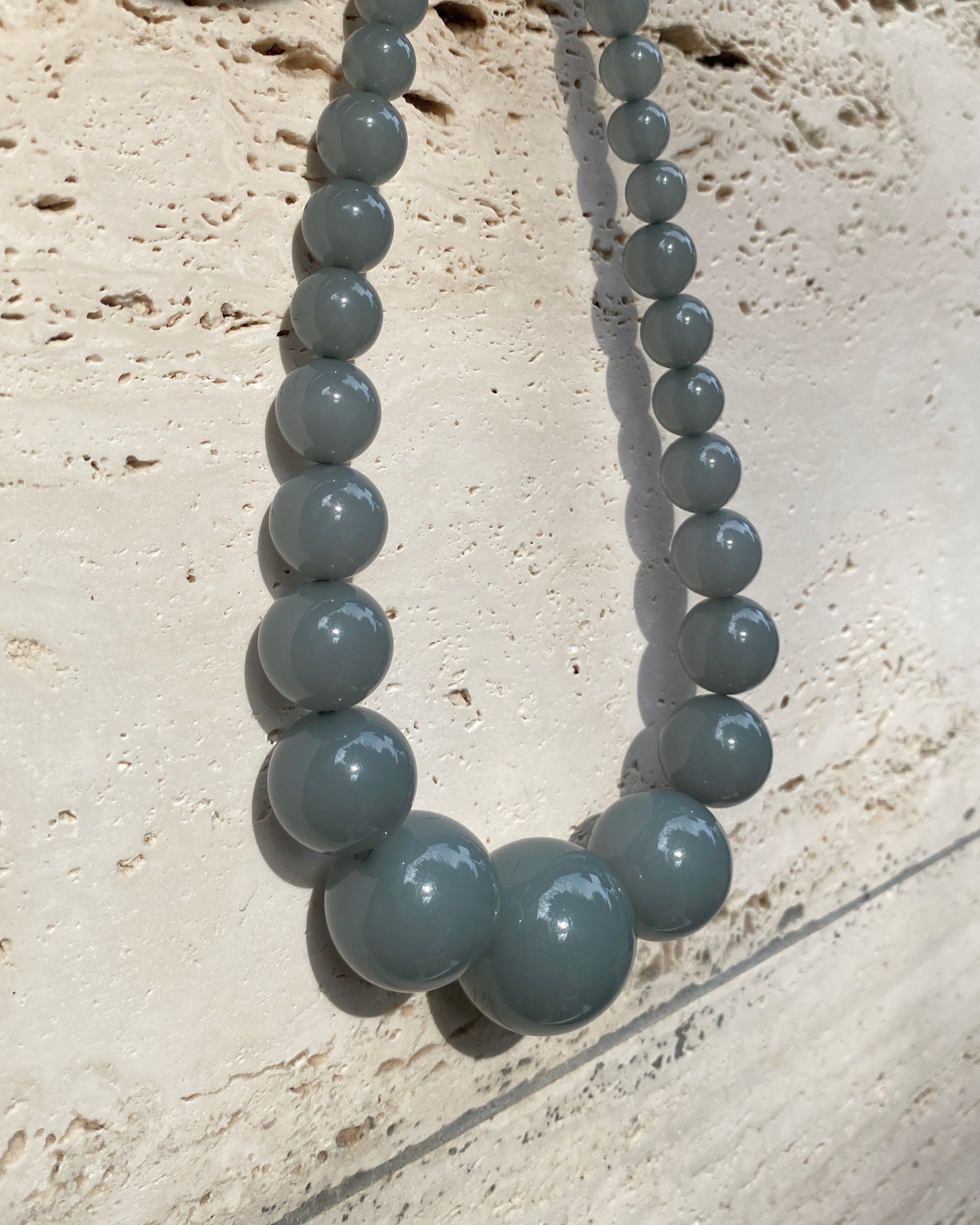 A beaded necklace with big  graduated  eucalyptus coloured beads  displayed on a stone wall. made in denmark by lemonade ltd