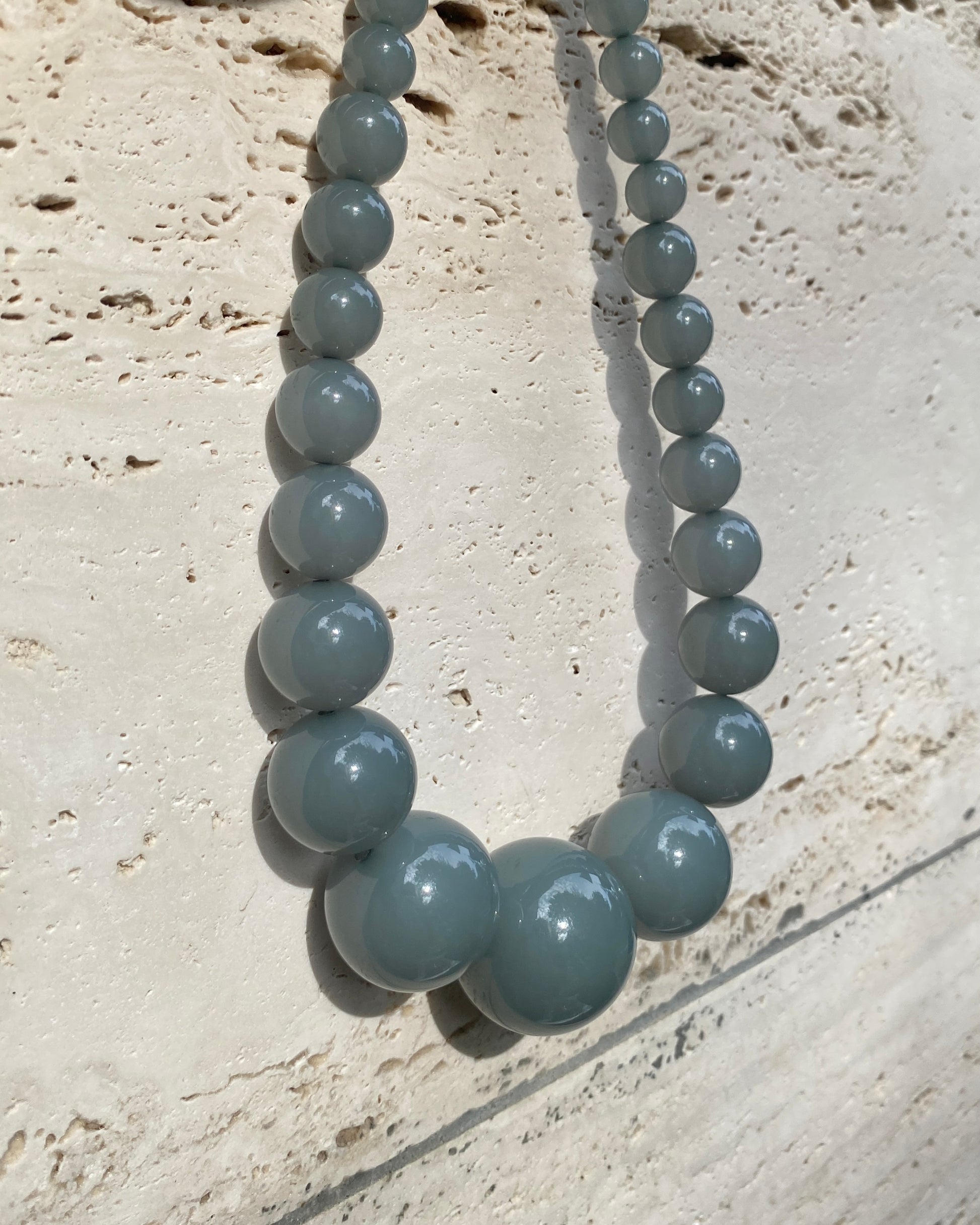 A beaded necklace with big  graduated  eucalyptus coloured beads  displayed on a stone wall. made in denmark by lemonade ltd