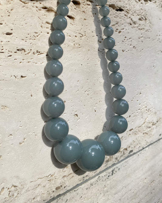 A beaded necklace with big  graduated  eucalyptus coloured beads  displayed on a stone wall. made in denmark by lemonade ltd