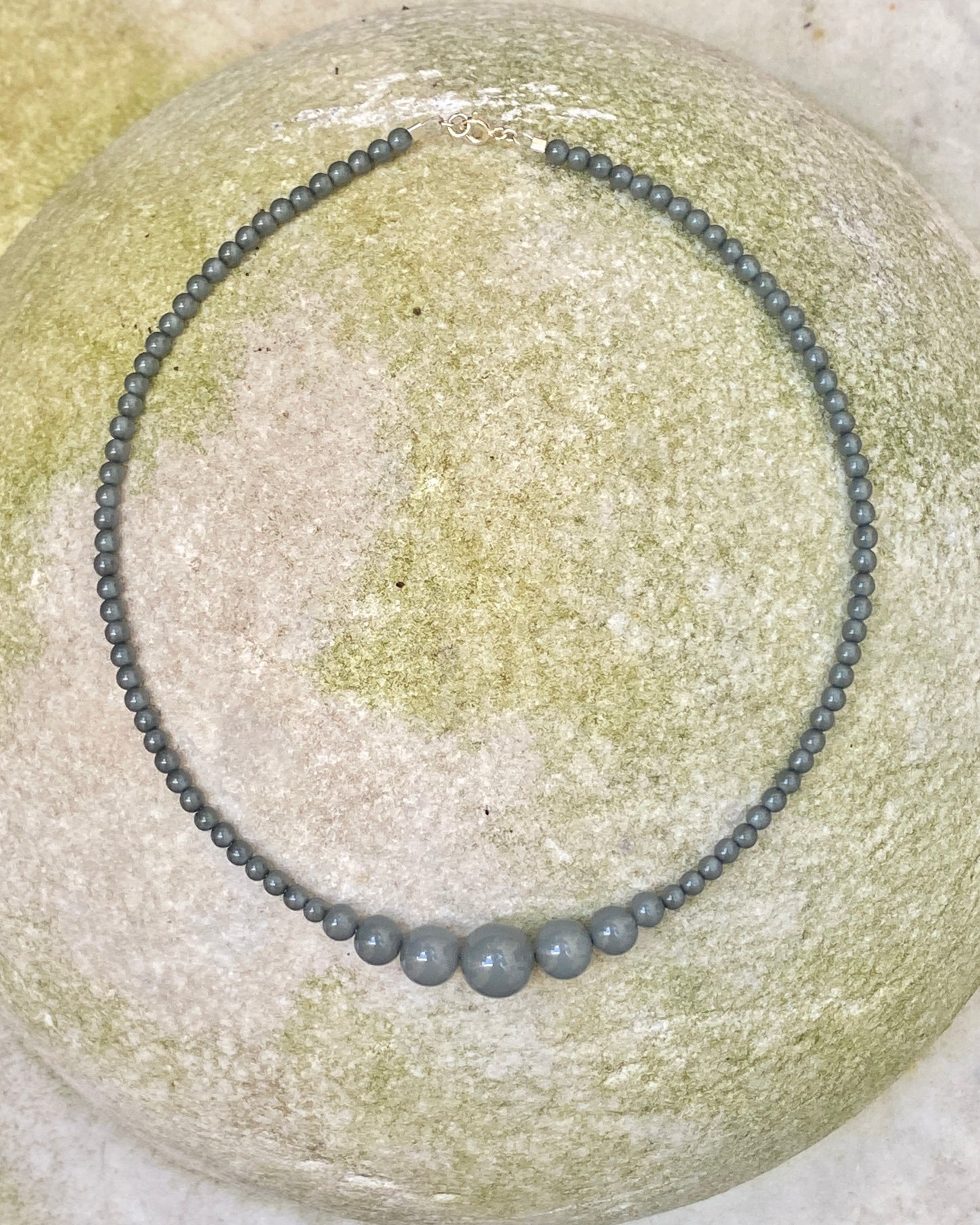 A beaded necklace with small dark eucalyptus coloured beads and three larger matching beads at the front, displayed on a stone. made in denamrk by lemonade ltd