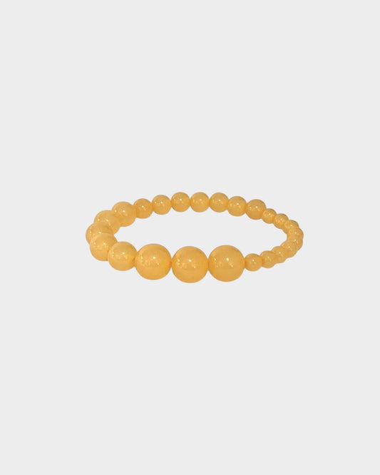 A  beaded stretch bracelet in honey-yellow colour with alternating large and small polished round resin beads, made by lemonade ltd. Made in copenhagen denmark