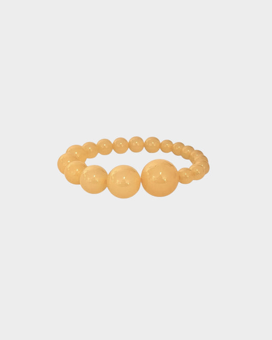 A  beaded stretch bracelet in honey yellow colour with alternating large and small polished round resin beads, made by lemonade ltd. Made in copenhagen denmark
