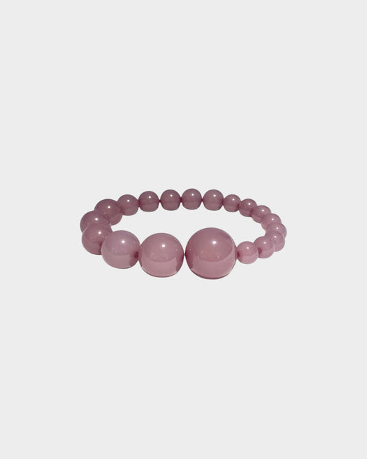 A  beaded stretch bracelet in plum colour with alternating large and small polished round resin beads, made by lemonade ltd. Made in copenhagen denmark