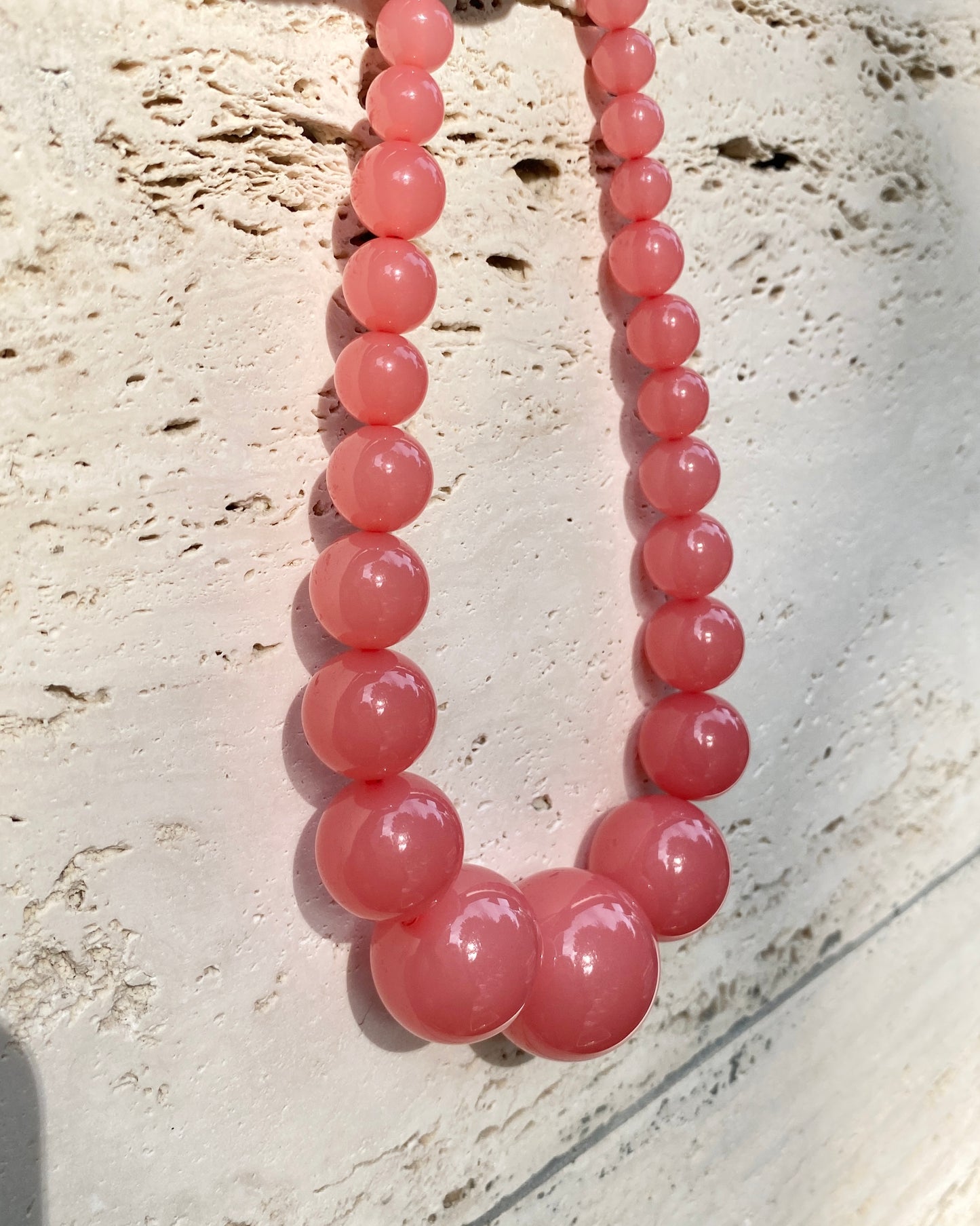 A pink beaded lemonade necklace made of smooth, polished round beads, displayed against a textured travetin background. made in denmark