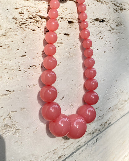 A pink beaded lemonade necklace made of smooth, polished round beads, displayed against a textured travetin background. made in denmark