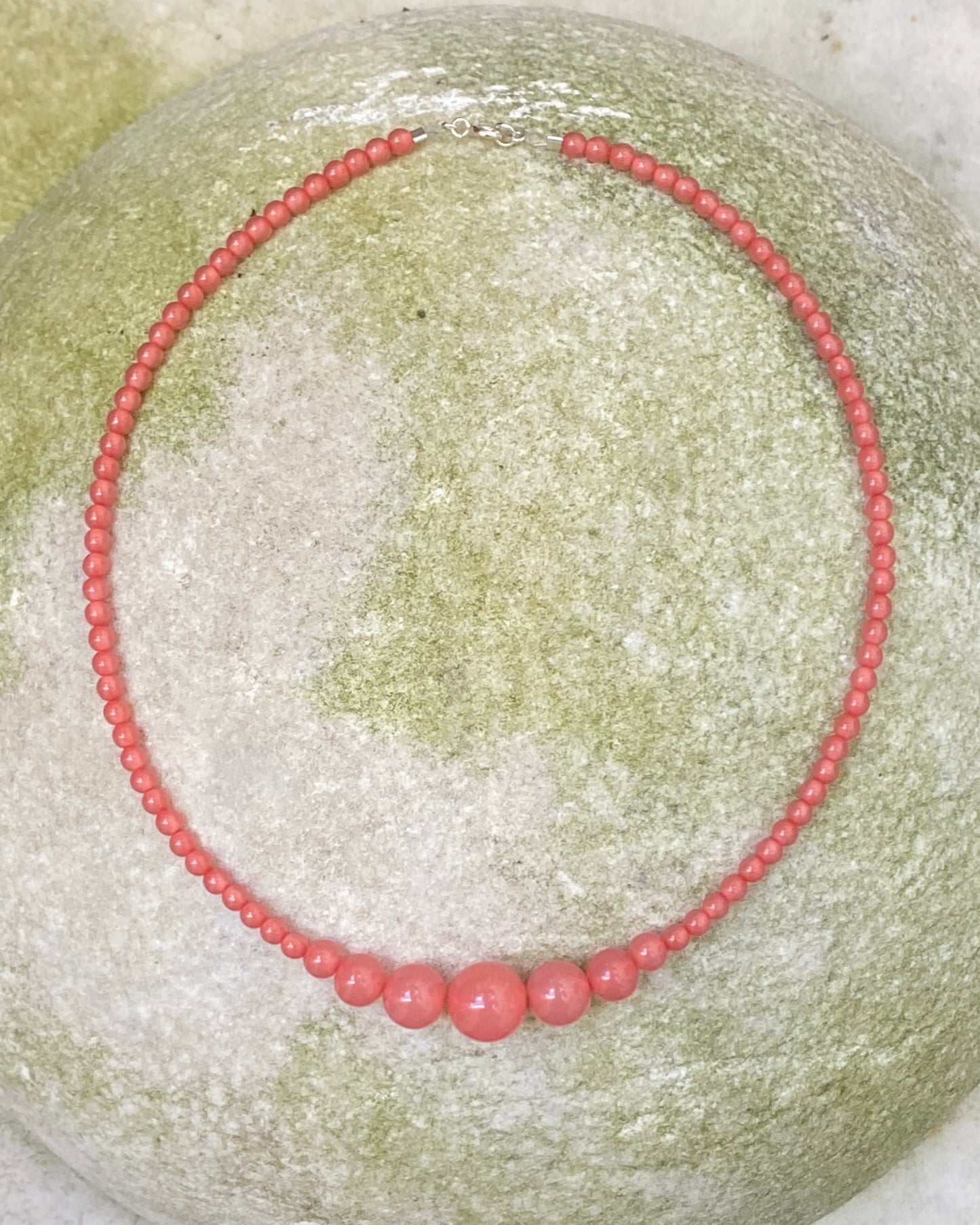 A rhubarb coloured beaded necklace from lemonade ltd with graduated beads, displayed on a stone. made in denmark