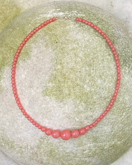 A rhubarb coloured beaded necklace from lemonade ltd with graduated beads, displayed on a stone. made in denmark